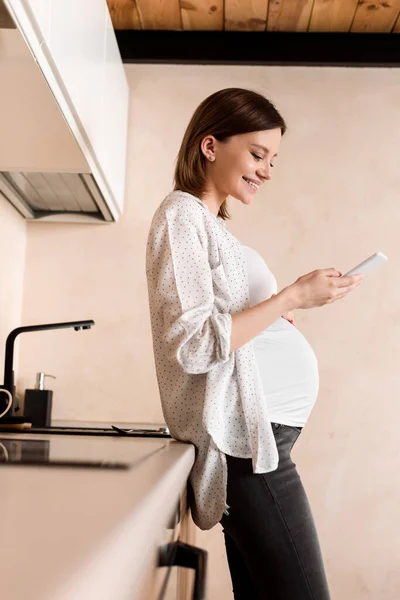Visão lateral da mulher grávida feliz usando smartphone — Fotografia de Stock