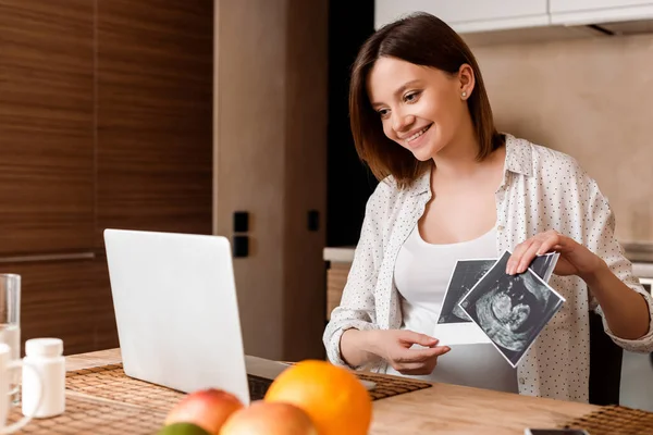 Вибірковий фокус весела вагітна жінка, що показує ультразвукові фотографії, маючи відеодзвінок — стокове фото