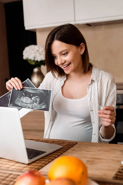 Selective focus of happy pregnant woman showing ultrasound photos while having video call — Stock Photo