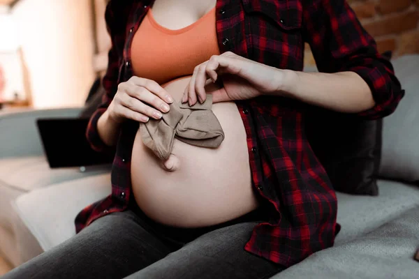 Обрезанный вид беременной женщины с детскими носками рядом с животом — стоковое фото