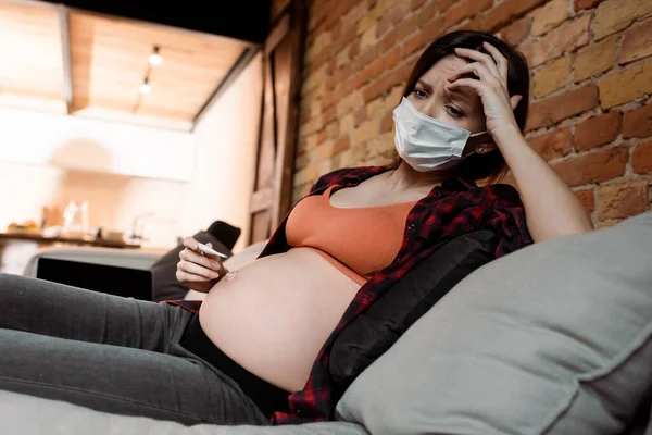 Больная и беременная женщина в медицинской маске держит цифровой термометр — стоковое фото