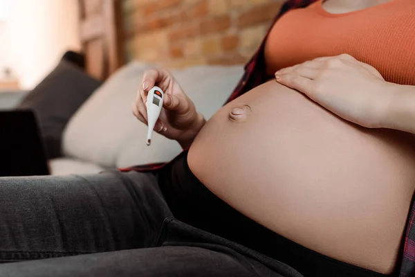 Vista recortada de la mujer enferma y embarazada sosteniendo termómetro digital - foto de stock
