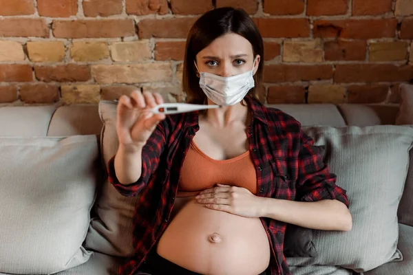 Вибірковий фокус вагітної жінки в медичній масці, що тримає цифровий термометр — стокове фото