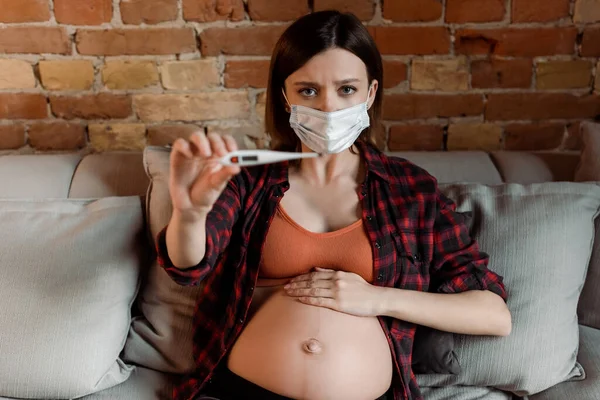 Selective focus of pregnant woman in medical mask holding digital thermometer — Stock Photo