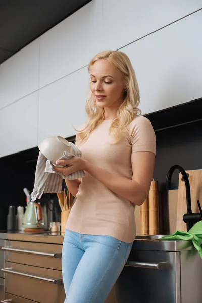 Приваблива, молода домогосподарка протирає чисту миску рушником на кухні — стокове фото