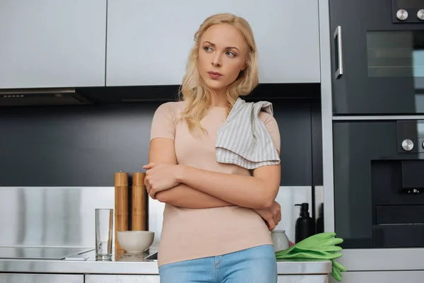 Bouleversé femme au foyer avec serviette sur l'épaule debout dans la cuisine et regardant loin — Photo de stock