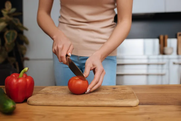 Vista recortada de la joven mujer cortando tomate fresco en la tabla de cortar - foto de stock