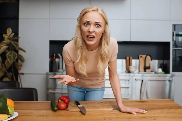 Femme en colère geste et regarder la caméra près des légumes frais dans la cuisine — Photo de stock