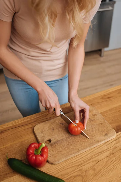 Cropped view of young woman cutting fresh tomato on chopping board — Stock Photo
