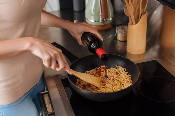 Vista recortada de la mujer vertiendo vino tinto en wok mientras prepara fideos tailandeses - foto de stock