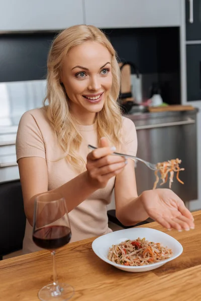 Smiling woman holding fork with thai noodles near glass of red wine — Stock Photo