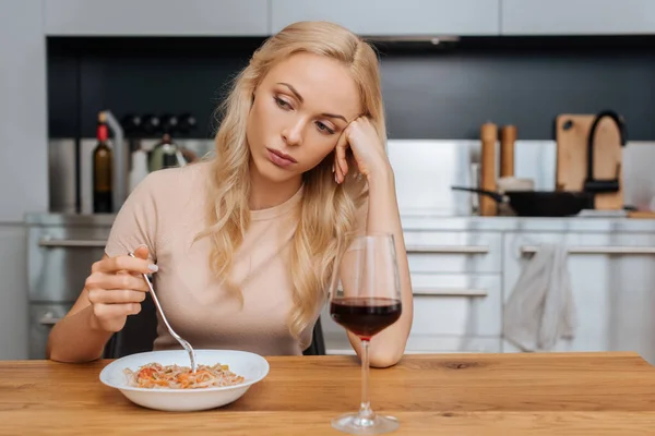 Upset woman holding fork near plate with thai noodles and glass of red wine — Stock Photo