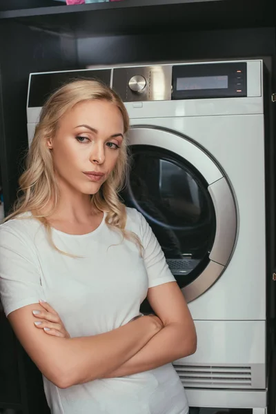 Desagradado dona de casa de pé com cruzados braços perto de máquina de lavar roupa — Fotografia de Stock