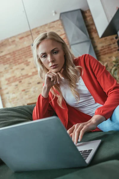 Thoughtful freelancer looking at laptop while holding hand near chin — Stock Photo