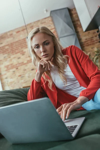 Nachdenklicher Freiberufler blickt auf Laptop, während er die Hand am Kinn hält — Stockfoto