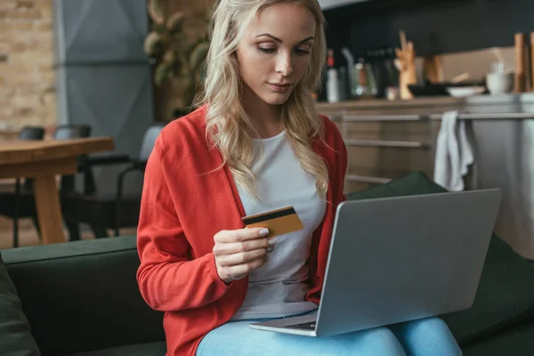 Уважна молода жінка тримає кредитну картку при використанні ноутбука — стокове фото