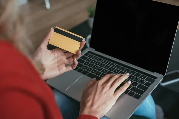 Vue recadrée de la femme en utilisant un ordinateur portable avec écran vierge tout en tenant la carte de crédit — Photo de stock