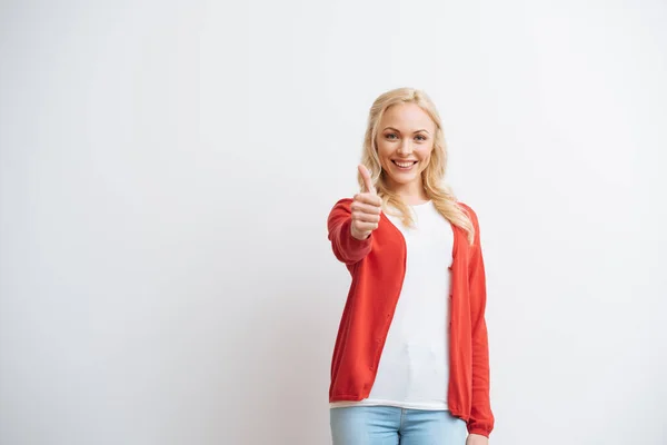 Cheerful blonde girl showing thumb up while smiling at camera isolated on white — Stock Photo