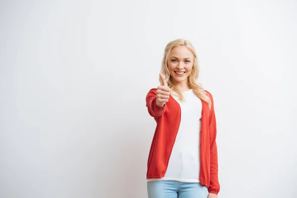 Alegre rubia chica mostrando el pulgar hacia arriba mientras sonríe a la cámara aislado en blanco - foto de stock