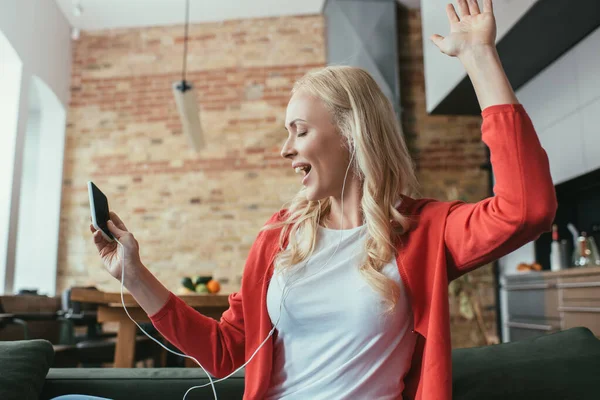 Felice donna in cuffia che canta ad occhi chiusi mentre tiene lo smartphone — Foto stock