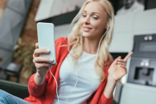 Enfoque selectivo de la mujer en los auriculares que muestran gesto de idea mientras mira el teléfono inteligente - foto de stock