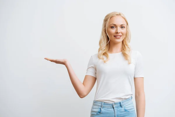 Mujer rubia sonriente de pie con el brazo abierto y mirando a la cámara aislada en blanco - foto de stock