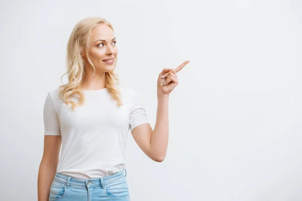 Lächelndes Mädchen, das wegschaut und mit dem Finger auf Weiß zeigt — Stockfoto