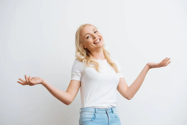 Cheerful blonde woman smiling at camera while standing with open arms isolated on white — Stock Photo