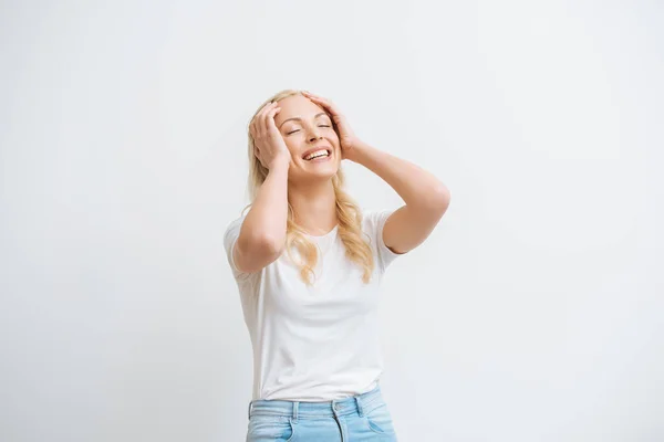 Excitée fille toucher la tête tout en riant avec les yeux fermés isolé sur blanc — Photo de stock