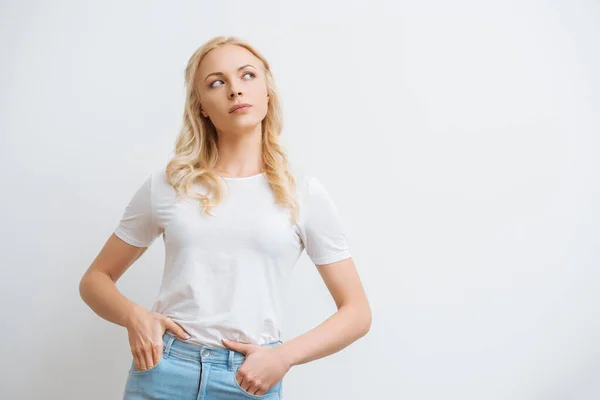 Thoughtful young woman looking away while standing with hands in pockets isolated on white — Stock Photo