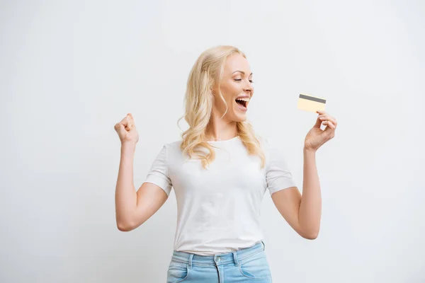 Mujer feliz mostrando gesto ganador mientras mantiene la tarjeta de crédito aislada en blanco - foto de stock