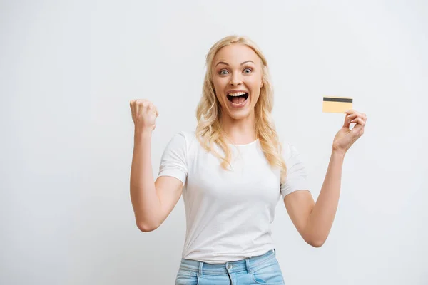 Excited woman showing winner gesture while holding credit card isolated on white — Stock Photo