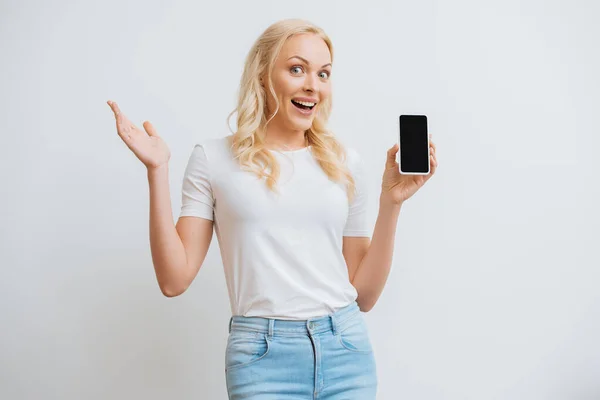 Aufgeregte Frau zeigt Smartphone mit leerem Bildschirm, während sie die Kamera isoliert auf Weiß betrachtet — Stockfoto