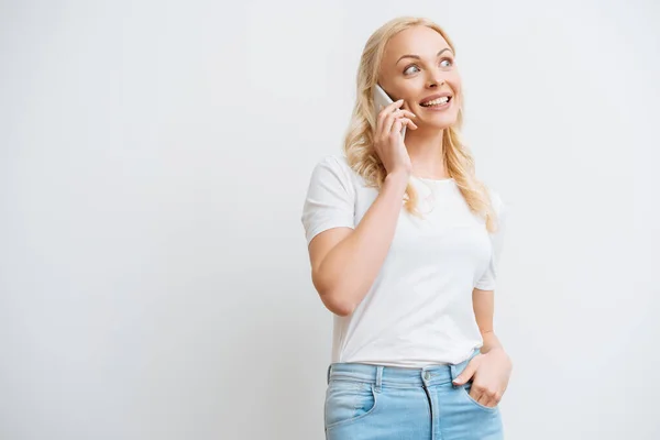 Mujer emocionada hablando en el teléfono inteligente mientras está de pie con la mano en el bolsillo aislado en blanco - foto de stock