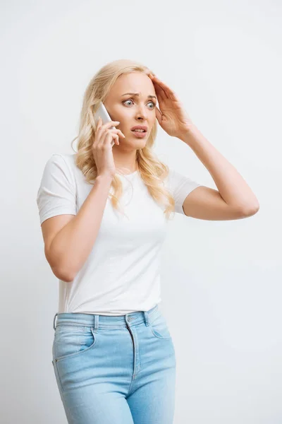 Mujer conmocionada tocando la cabeza mientras habla en el teléfono inteligente aislado en blanco - foto de stock
