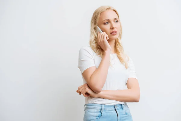 Засмучена блондинка говорить на смартфоні і дивиться ізольовано на білому — стокове фото