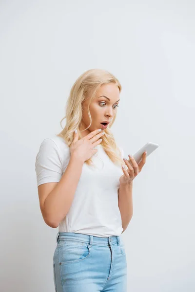 Menina chocada tocando queixo enquanto tem chamada de vídeo no smartphone isolado no branco — Fotografia de Stock