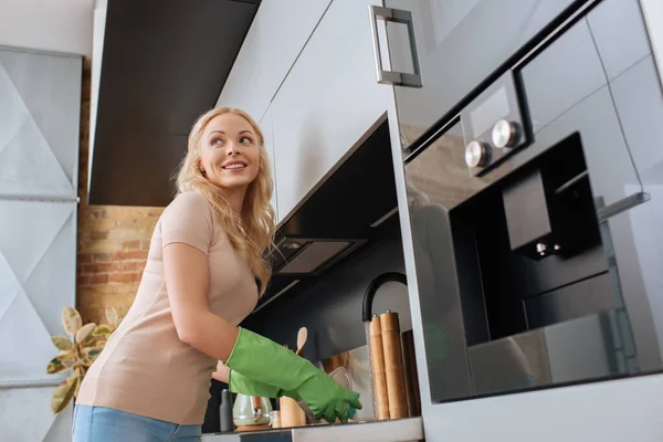 Ama de casa sonriente mirando hacia otro lado mientras lava platos en la cocina - foto de stock