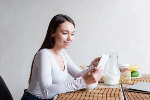 Glückliche Frau mit Smartphone und Kochlöffel mit leckeren Cornflakes — Stockfoto