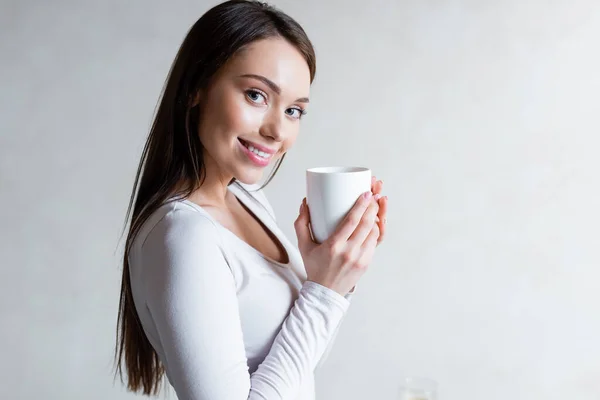 Cheerful girl holding cup of tea and smiling at home — Stock Photo