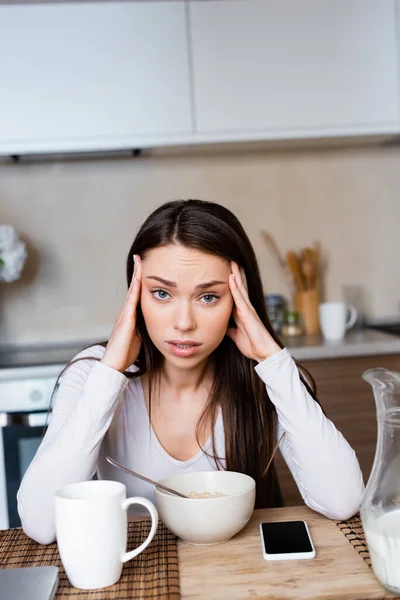 Upset girl touching head near bowl, jug and smartphone with blank screen — Stock Photo