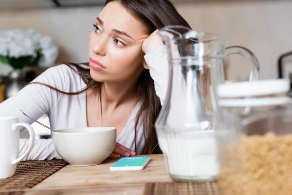 KYIV, UKRAINE - APRIL 29, 2020: selective focus of sad girl near bowl, jug, cup and smartphone with twitter app — Stock Photo