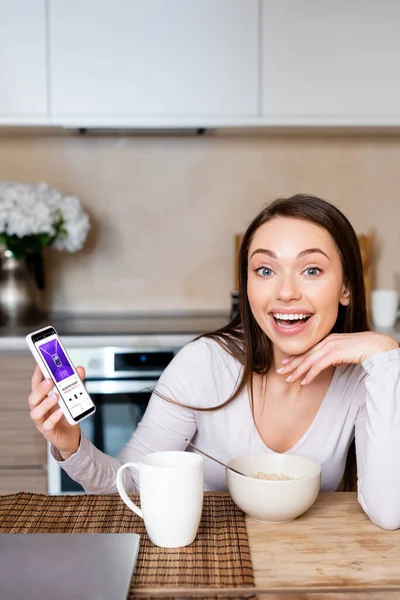 KYIV, UKRAINE - 29 de abril de 2020: mulher animada segurando smartphone com aplicativo de música de maçã perto do copo e da tigela — Fotografia de Stock