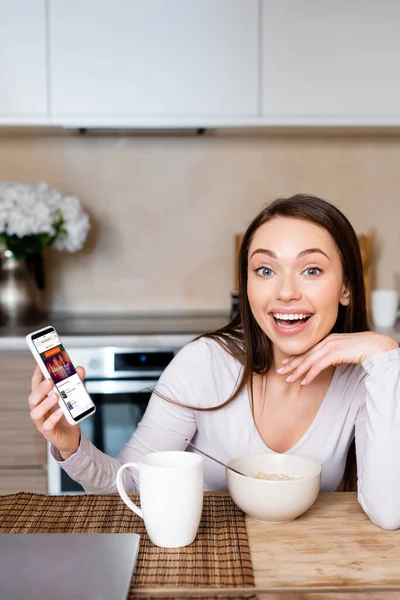 KYIV, UKRAINE - APRIL 29, 2020: excited woman holding smartphone with soundcloud app near cup and bowl — Stock Photo