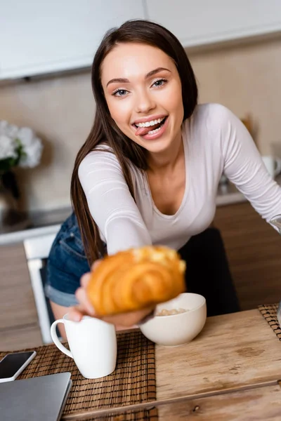 Selective focus of girl holding tasty croissant and sticking out tongue — Stock Photo
