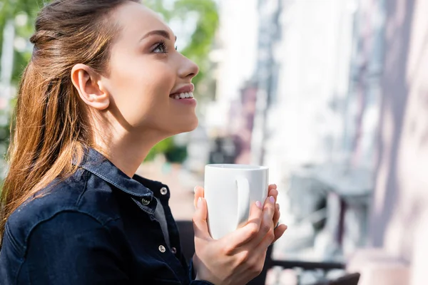 Vista lateral de la mujer alegre sosteniendo la taza de café fuera - foto de stock