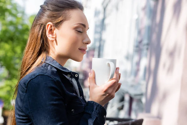 Seitenansicht einer glücklichen Frau mit geschlossenen Augen, die eine Tasse Kaffee draußen hält — Stockfoto
