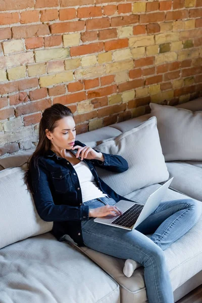 Pensive freelancer using laptop while sitting on sofa — Stock Photo