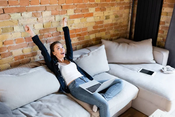 Freelance excité avec les mains au-dessus de la tête près de l'ordinateur portable et tablette numérique avec écran blanc — Photo de stock