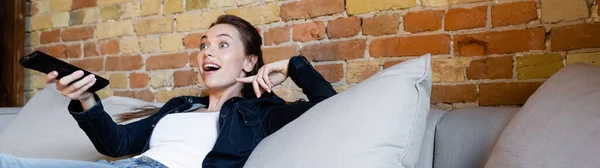 Panoramic crop of surprised girl holding remote controller — Stock Photo